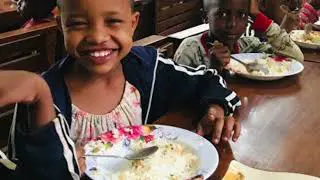 a young Maasai girl sitting at a table is happy while eating healthy food