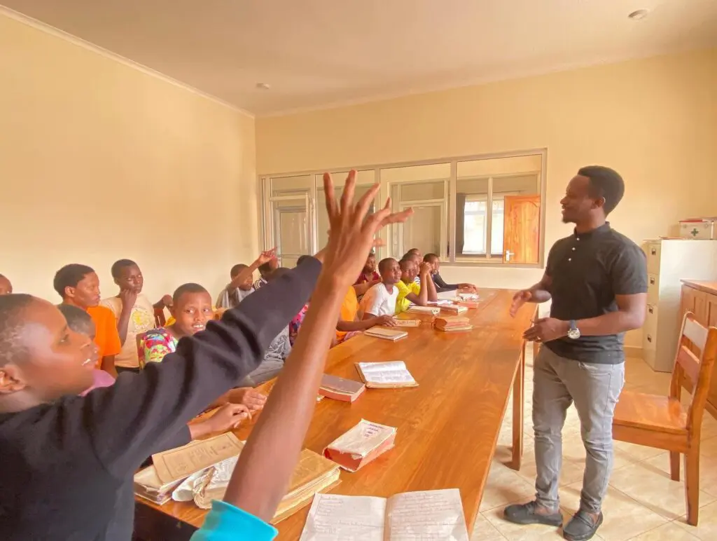 a pastor conducting a bible class for maasai girls who are raising their hands in particpation.