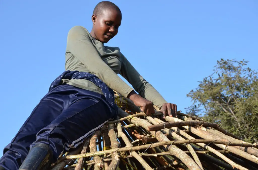 Neema tying sticks on the roof of one of the bomas