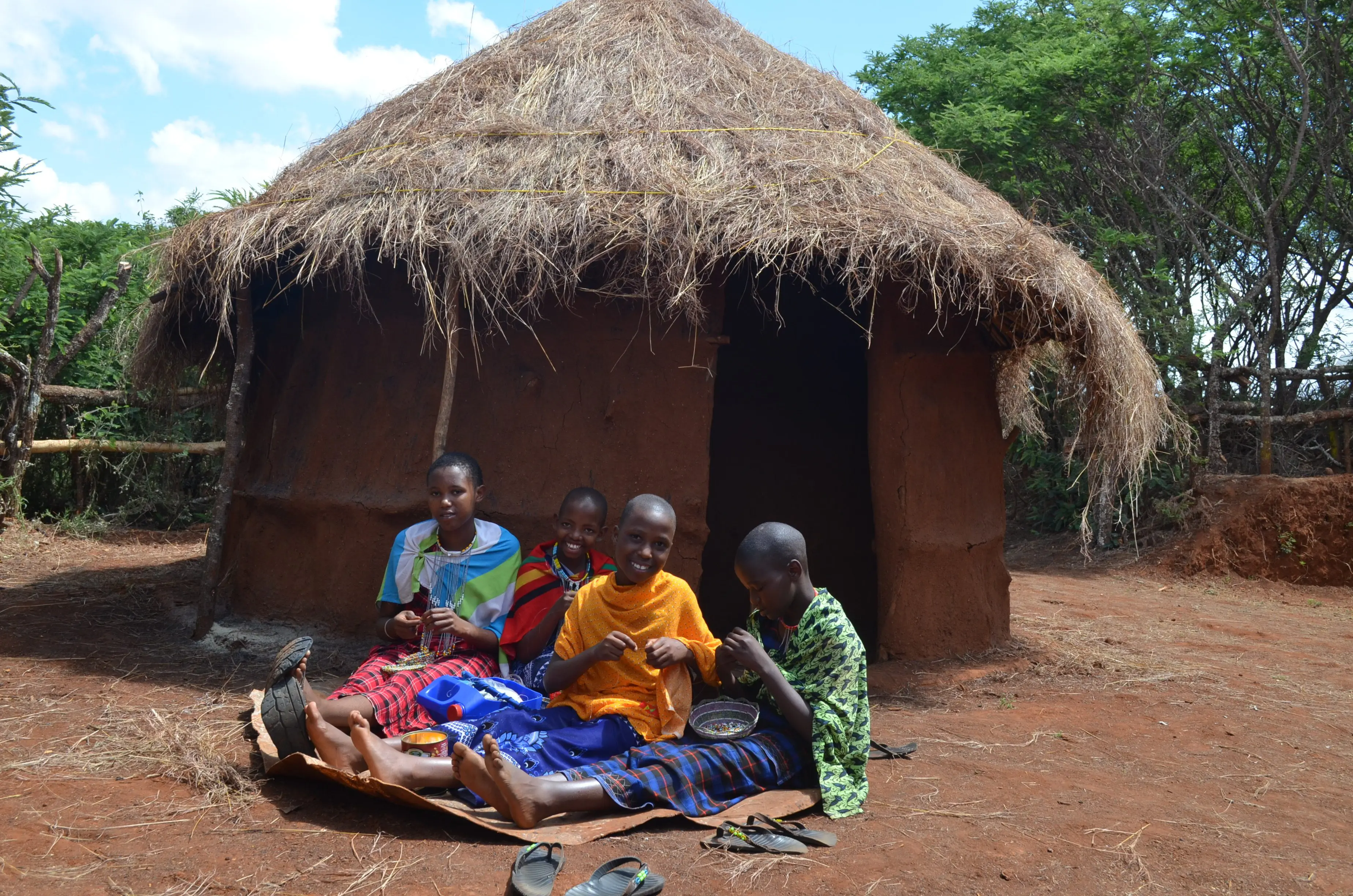 maasai girls sitting together doing beadwork in front a boma