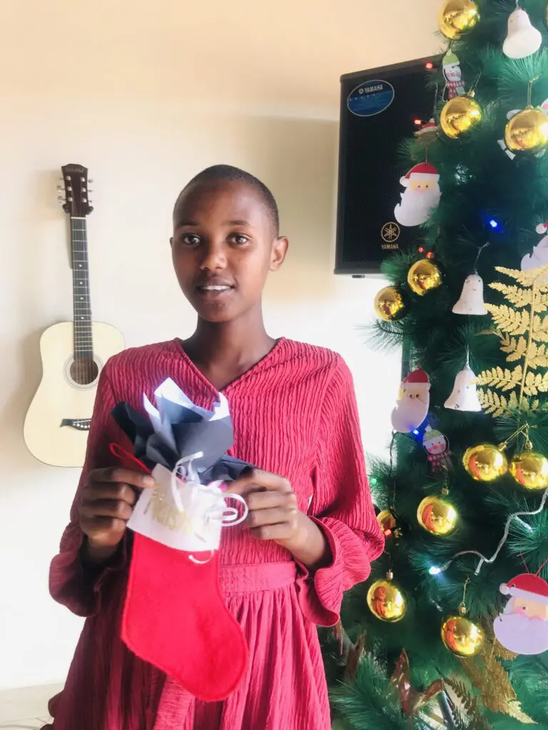 Rose holding a Christmas gift while standing in front of a Christmas tree