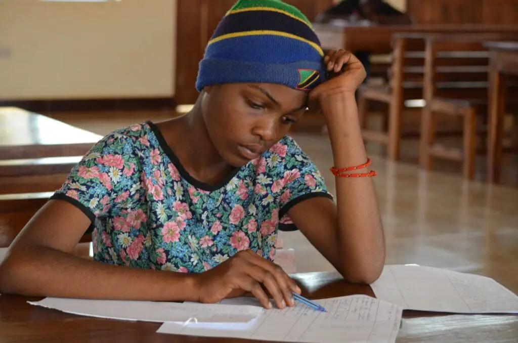 a Maasai girl sitting at a table writing on paper, breaking barriers for education access