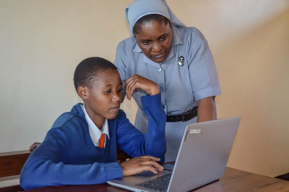Sister Silvia leaning over to help student with laptop.