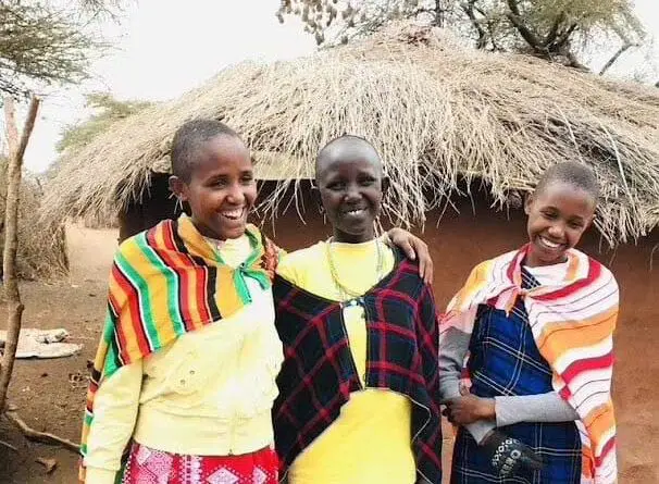 Empowering Maasai girls standing in front of a boma, highlighting the cultural and purposeful travel experience.