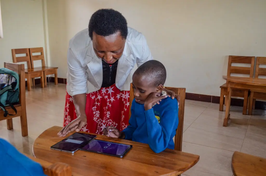 Mama Flora our lead teacher assisting student with tablet