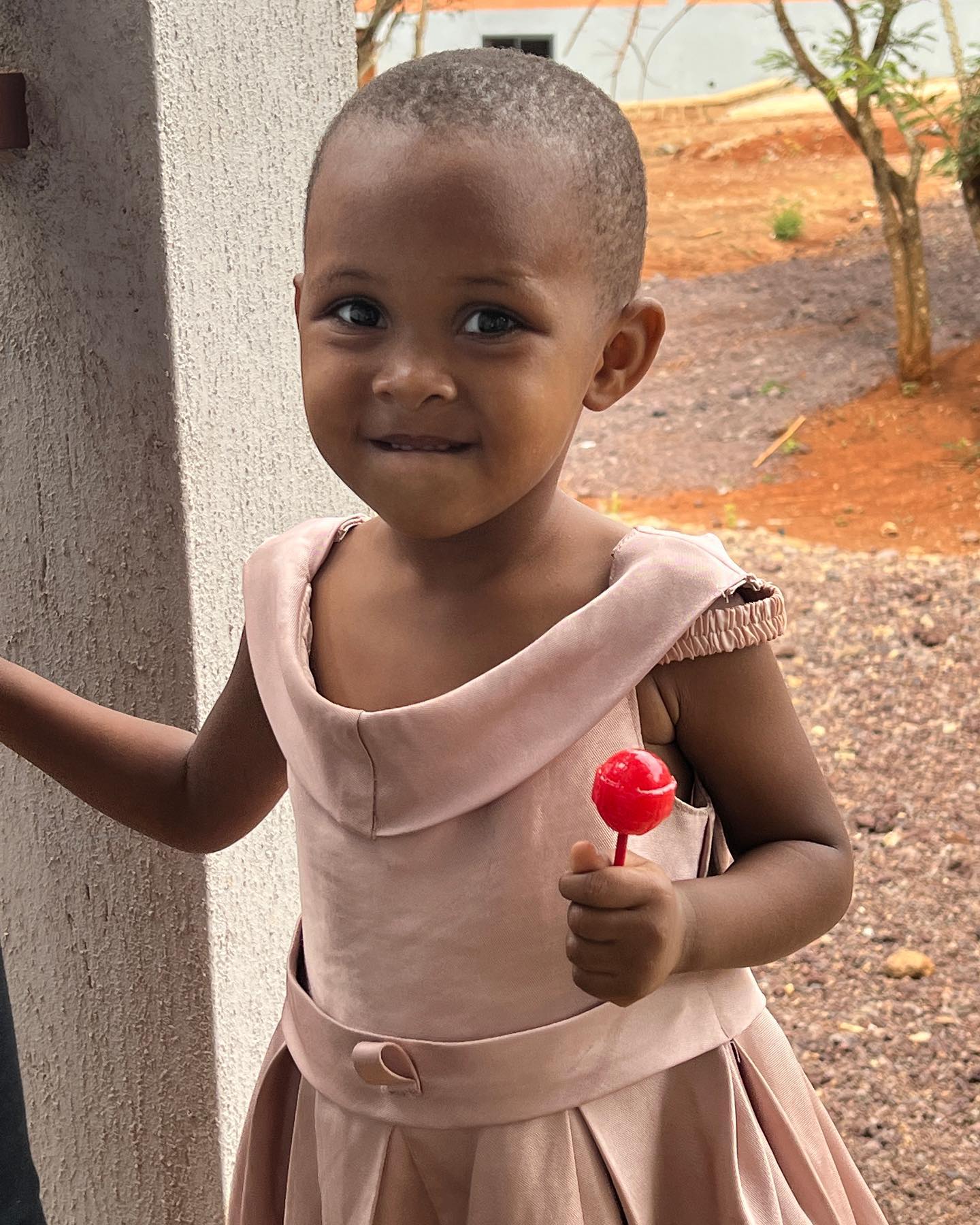 a young maasai girl in a pink dress holding a lollipop and smiling