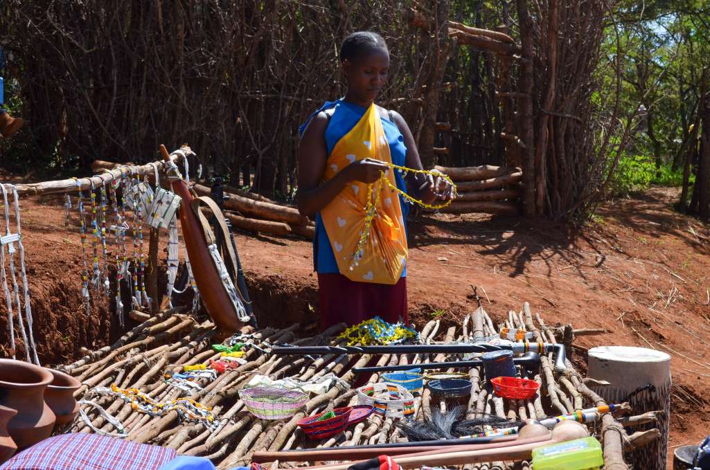 Maasai woman displaying her beadmaking on stick table, summer of growth demostration