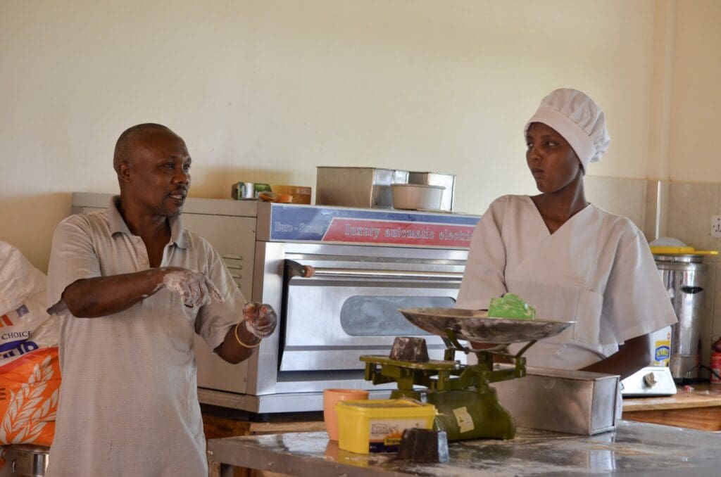 Maasai teen girl listening to ecolodge chef demostrating ingredient measurement scale.