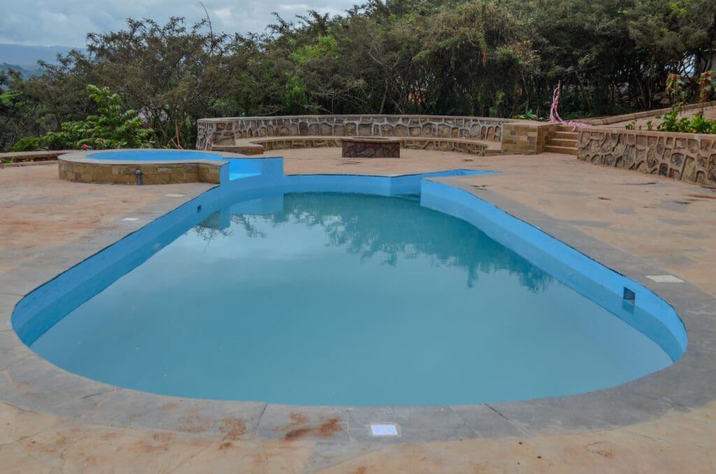 ecoLodge swimming pool with blue interior, surrounded by a stone deck and a low stone wall, with trees and cloudy sky in the background.