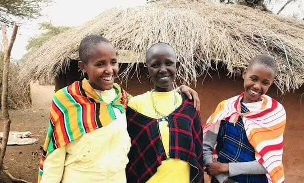 Empowering Maasai girls standing in front of a boma, highlighting the cultural and purposeful travel experience.
