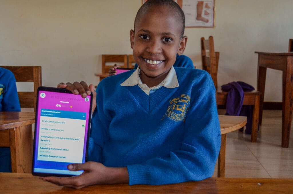Smiling Maasai girl holding tablet in classroom at MGRC