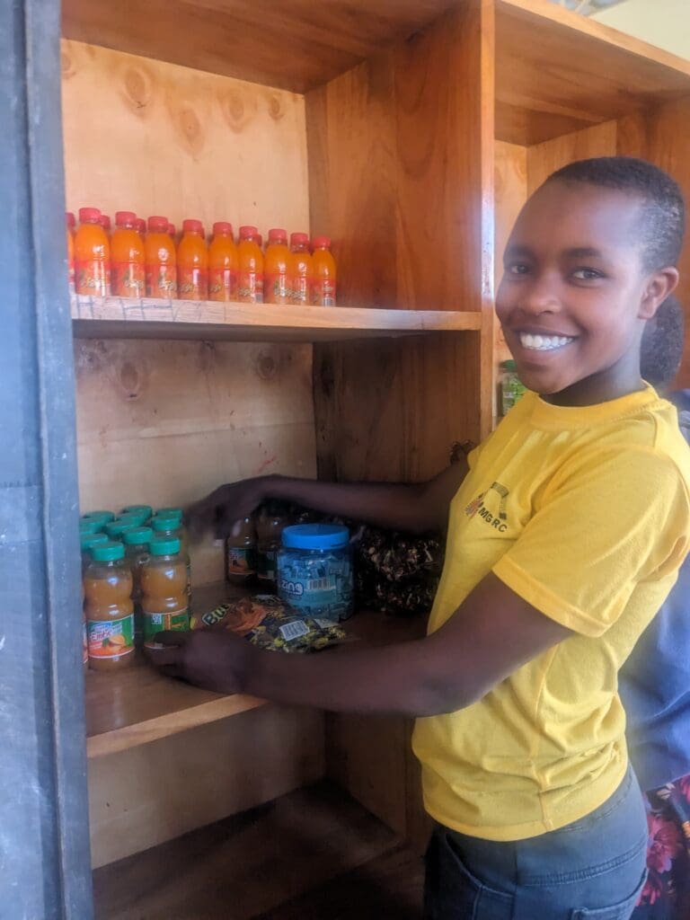 Young Maasai girl smiling while restocking the shelves at a shop.