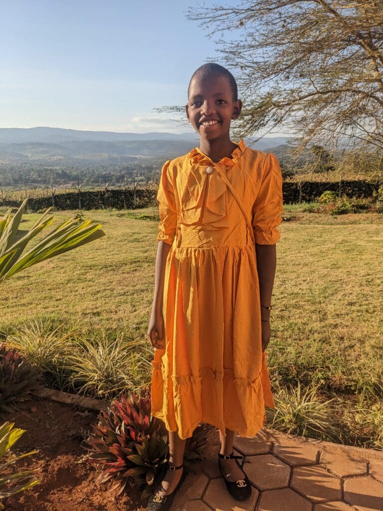 Young maasai girl in a yellow dress smiling with a reason to celebrate after speaking at tanzania parliment on women's rights.