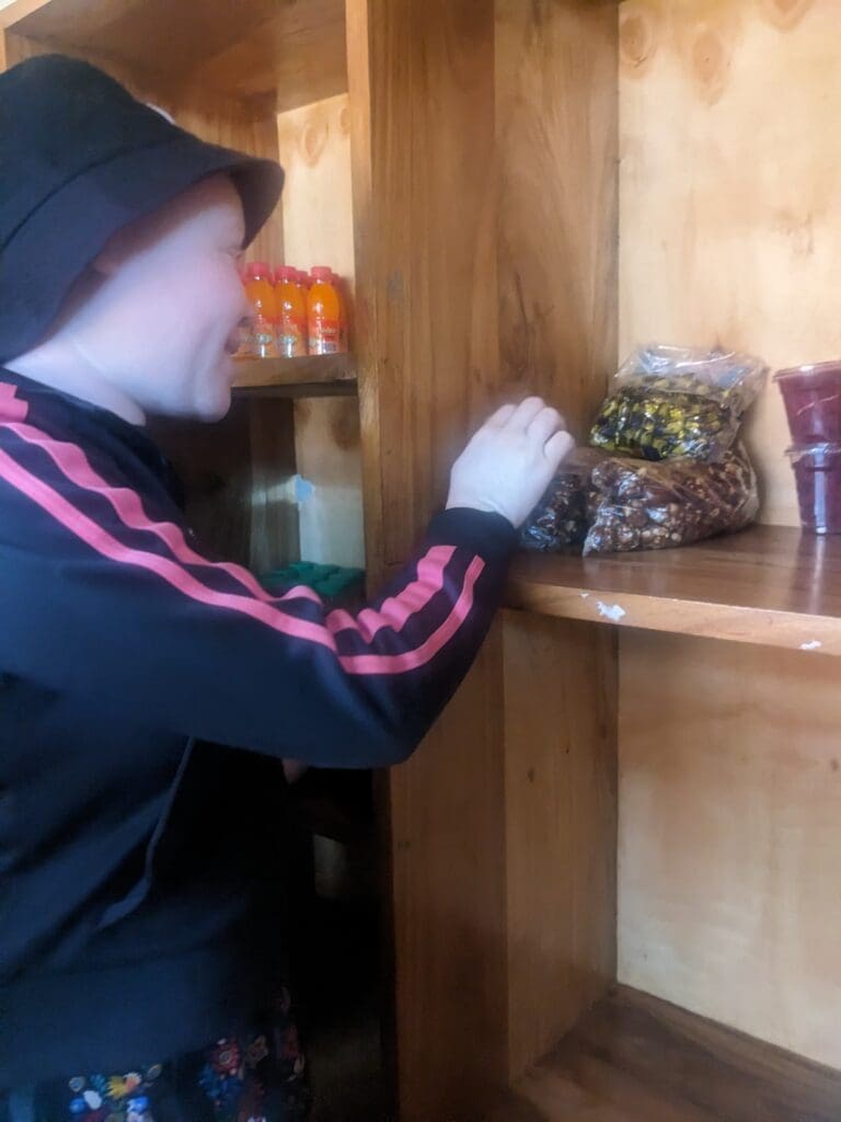 Young girl in wide brim hat placing store items on a shop shelf.
